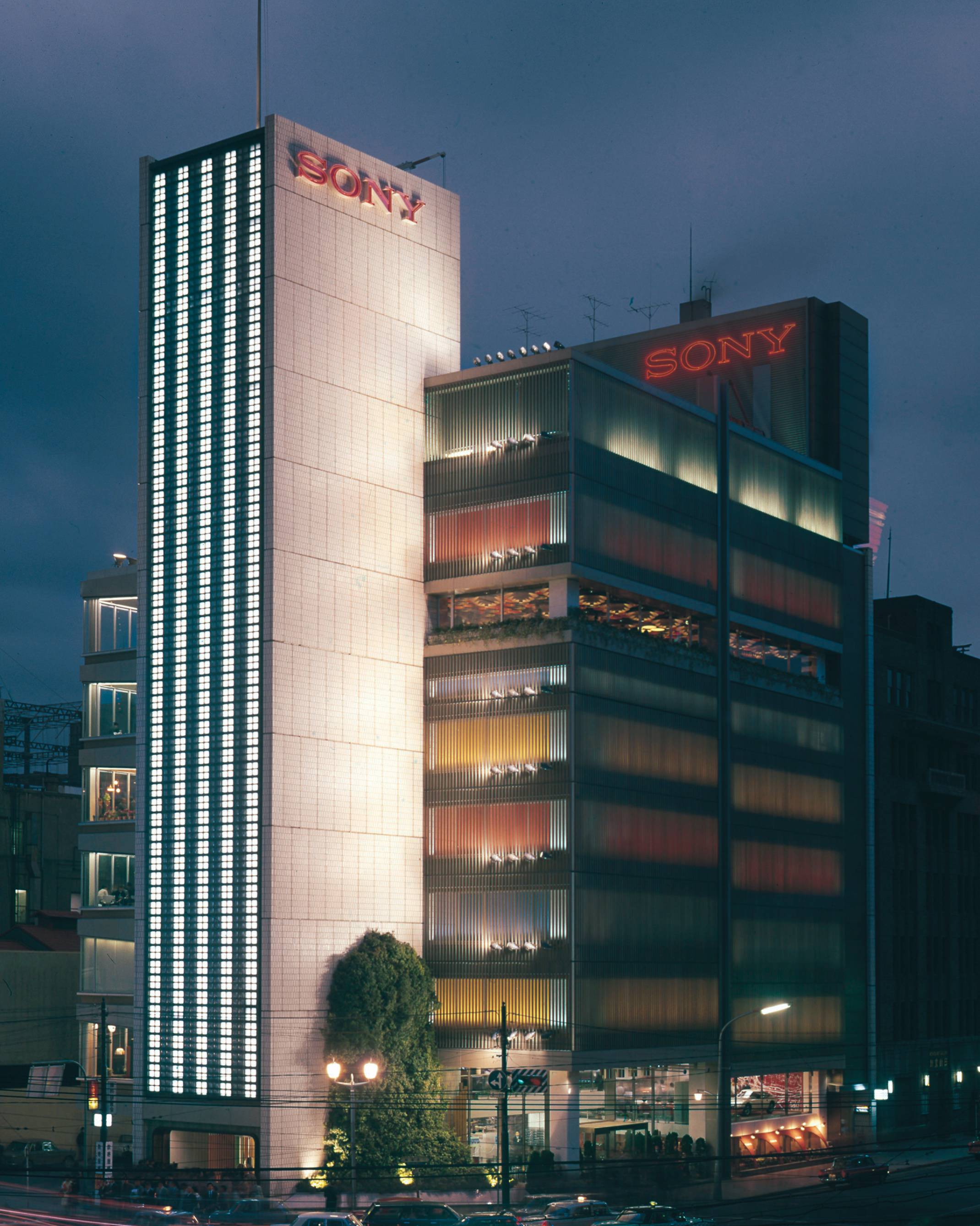 Sony Building exterior. Panoramic view of the Sony Building at night, beyond Sukiyabashi Crossing. A three-story-high Japanese andromeda tree has been planted in Sony Square (outdoor event space) in front facing the intersection.