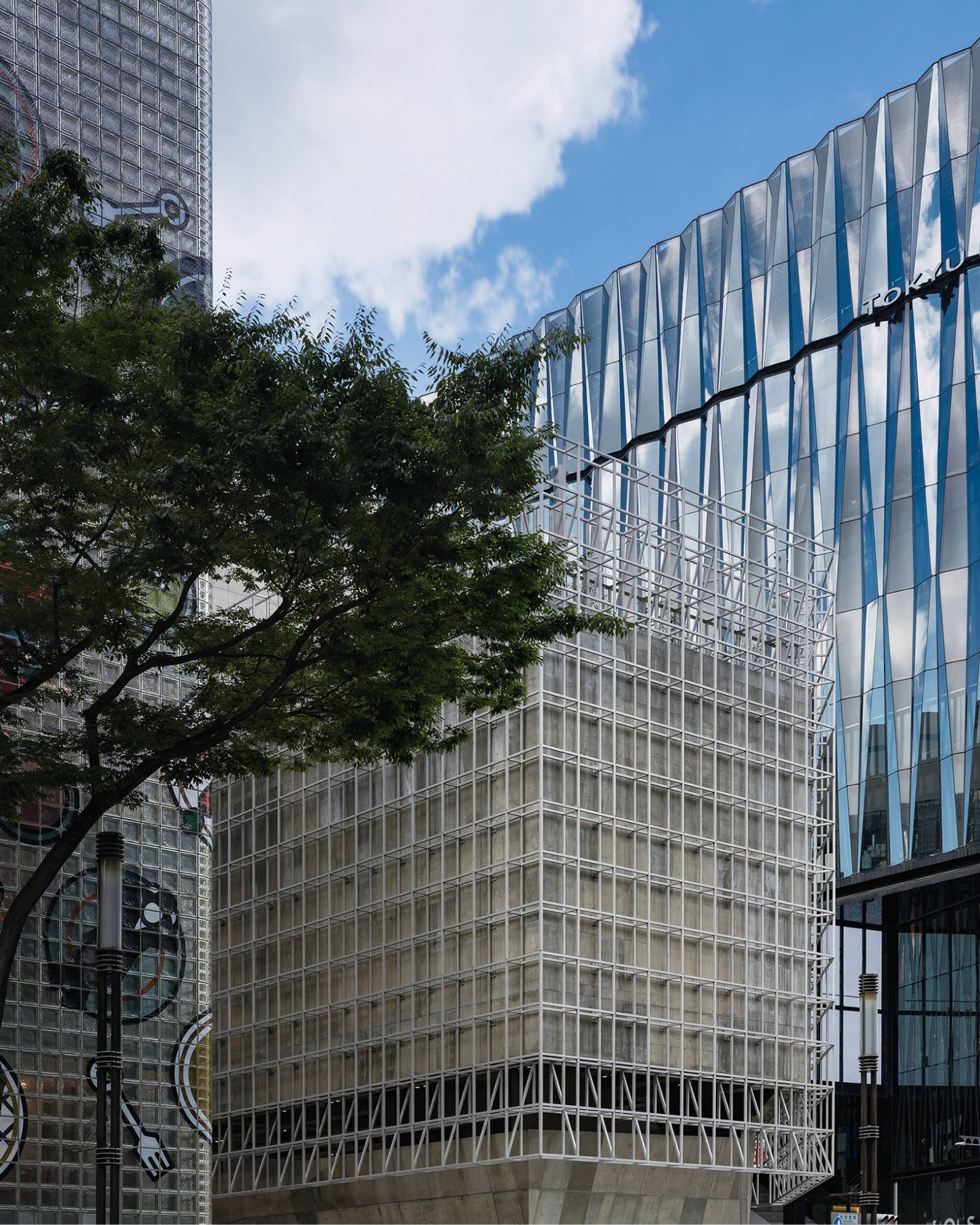 Exterior. Ginza Sony Park, with its low height and grid-like façade, is nestled between Maison Hermès and Tokyu Plaza Ginza. Trees line the street in front of it.