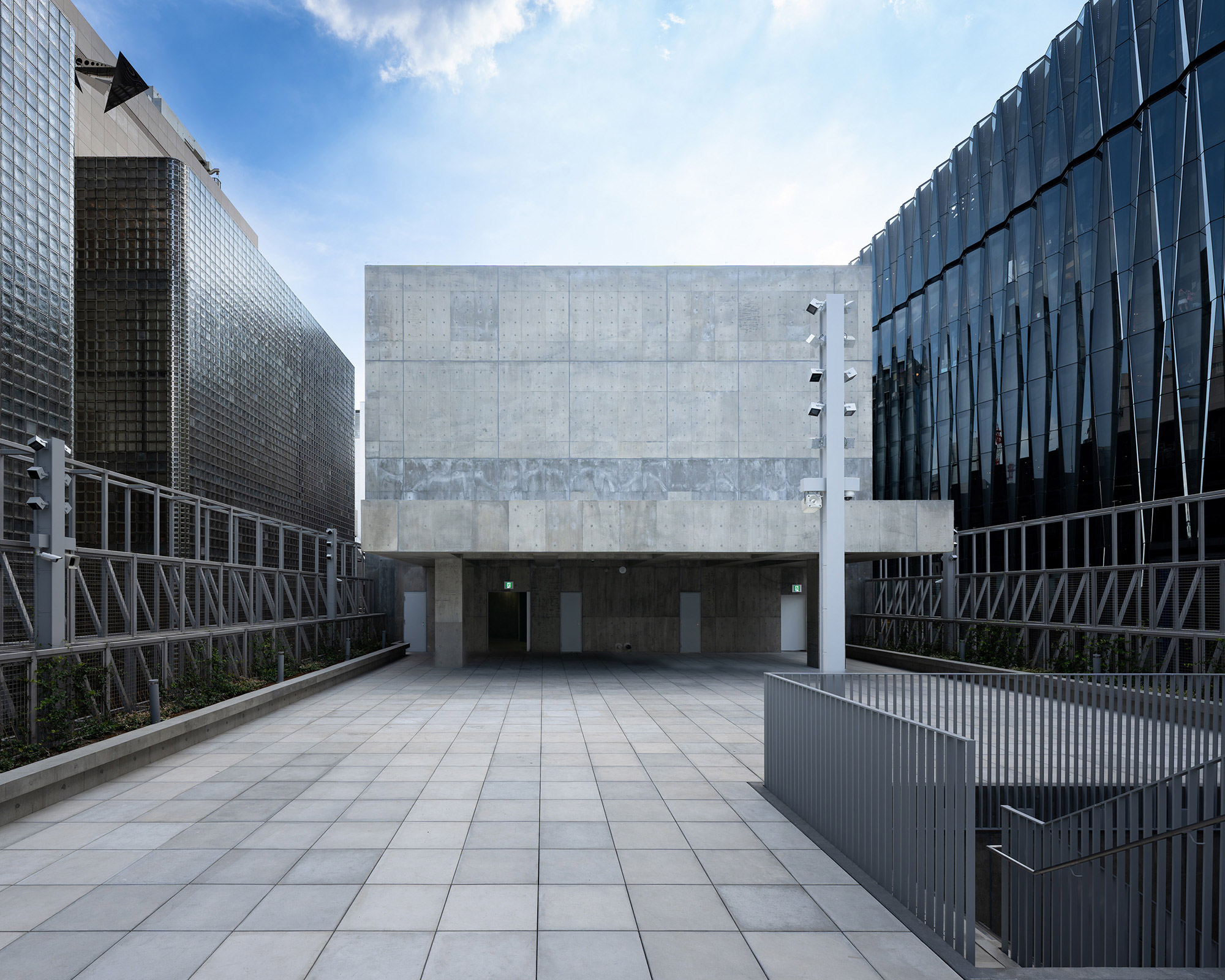 Exterior. The rooftop floor, nestled low compared to the surrounding buildings, with its concrete tower and pavilion beneath the blue sky.