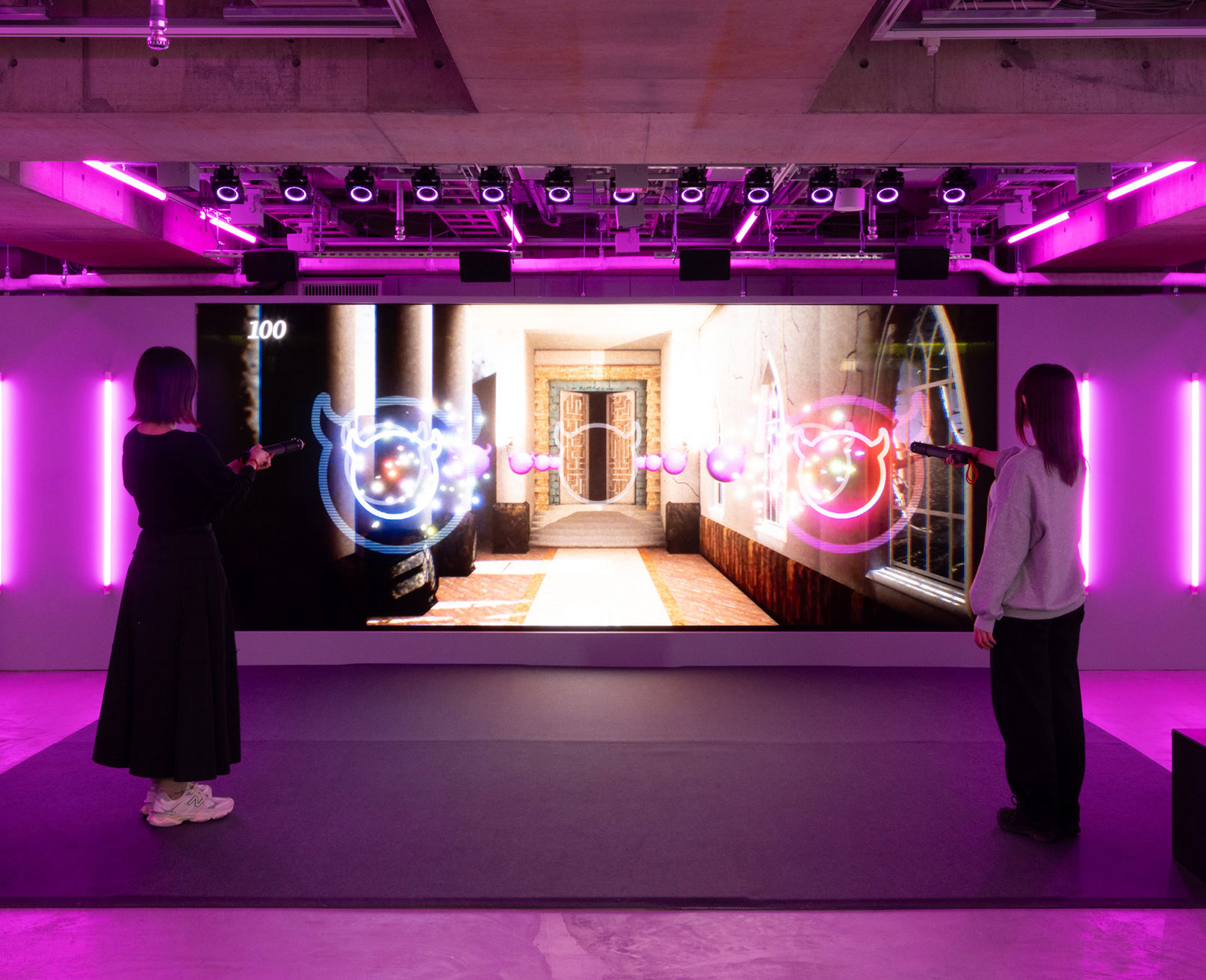Exhibit. Two visitors stand in front of a screen and play a digital shooting game.