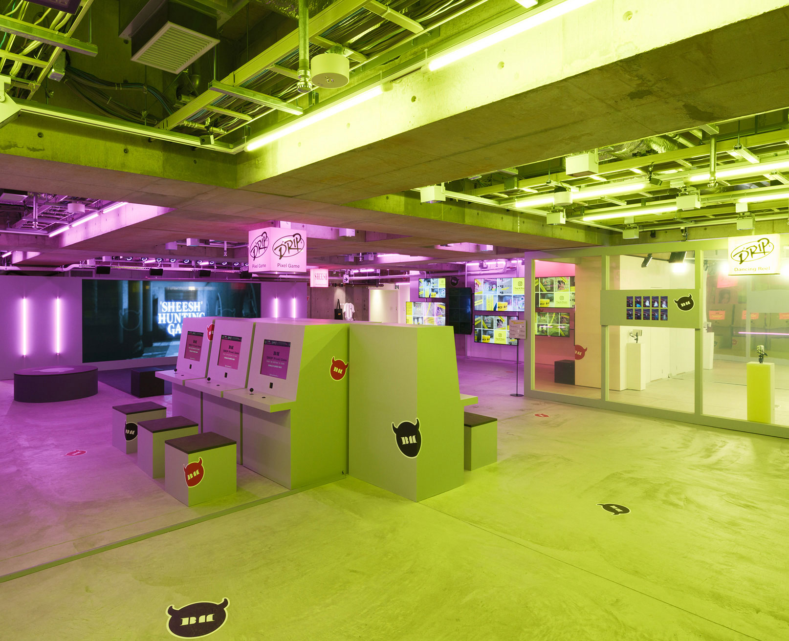 Exhibit. A space illuminated with pink and yellow lighting features a screen and interactive terminals for games.