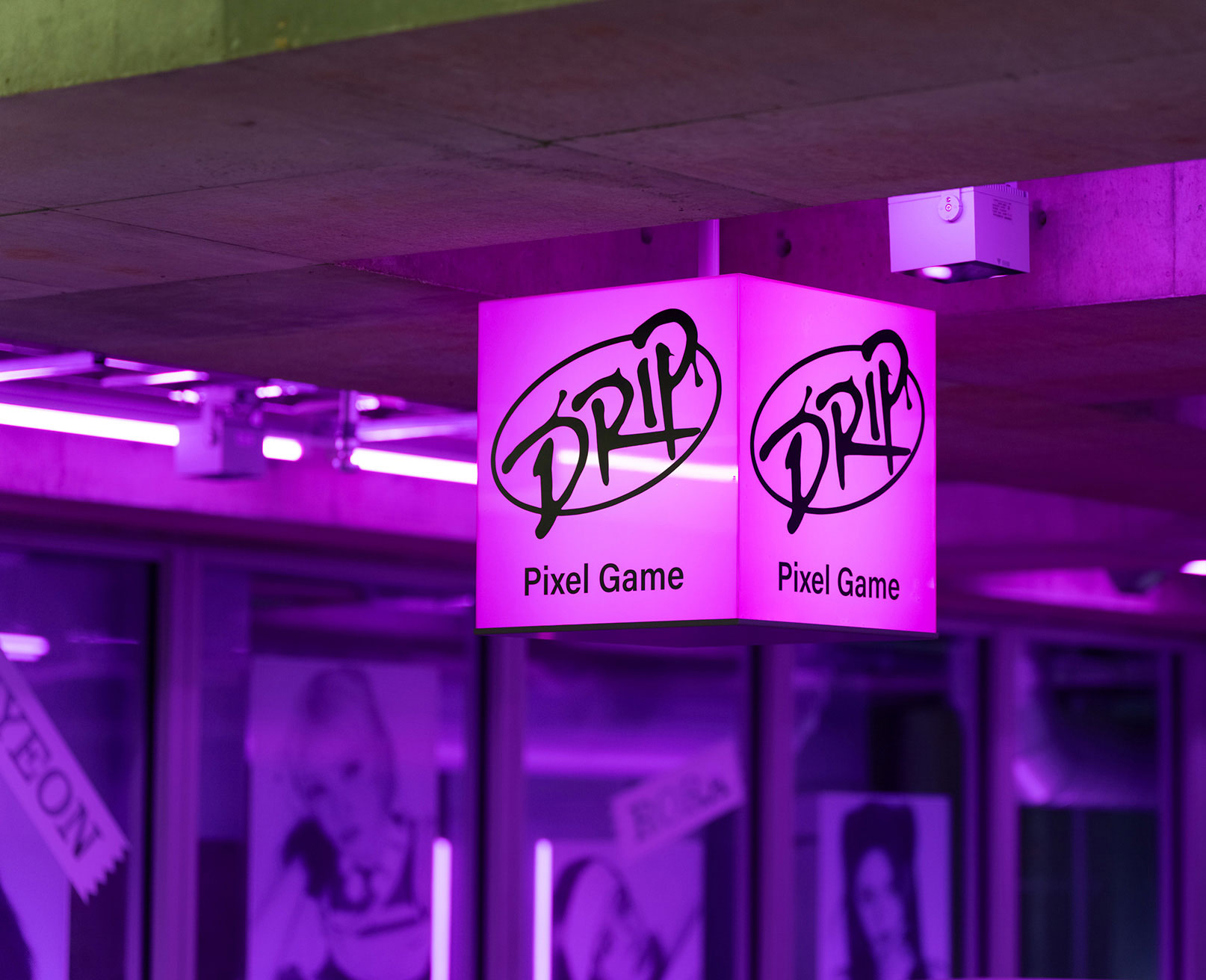 Exhibit. A glowing pink cube-shaped sign reading “DRIP Pixel Game,” hanging in a neon-lit space.