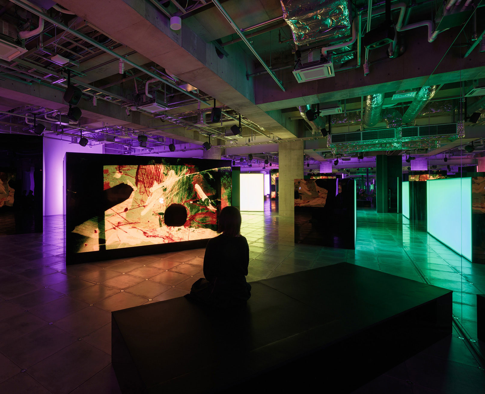Exhibit. A visitor sits on a bench in front of a screen displaying colorful animation.