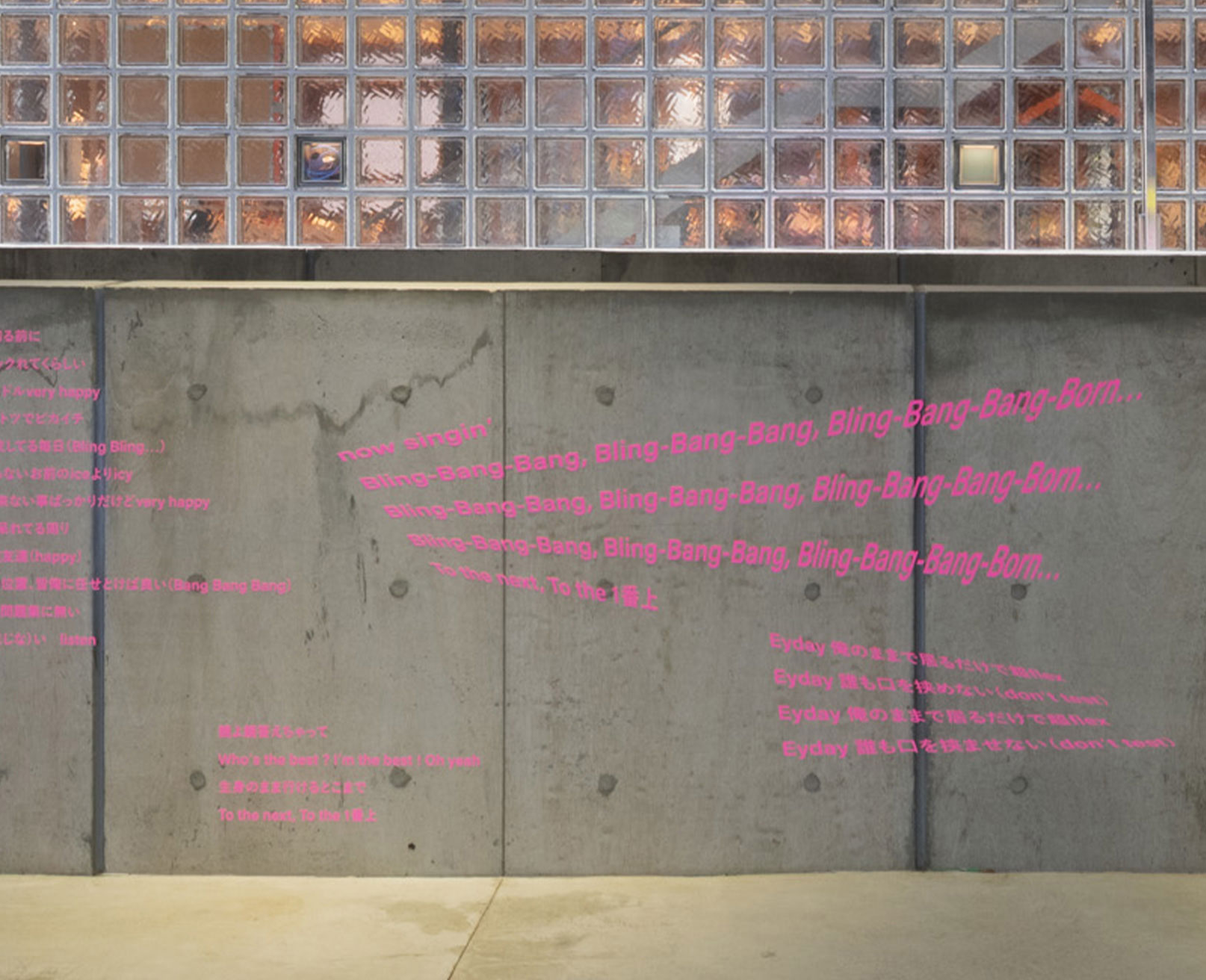 Exhibit. Pink lyrics are printed on a concrete wall.