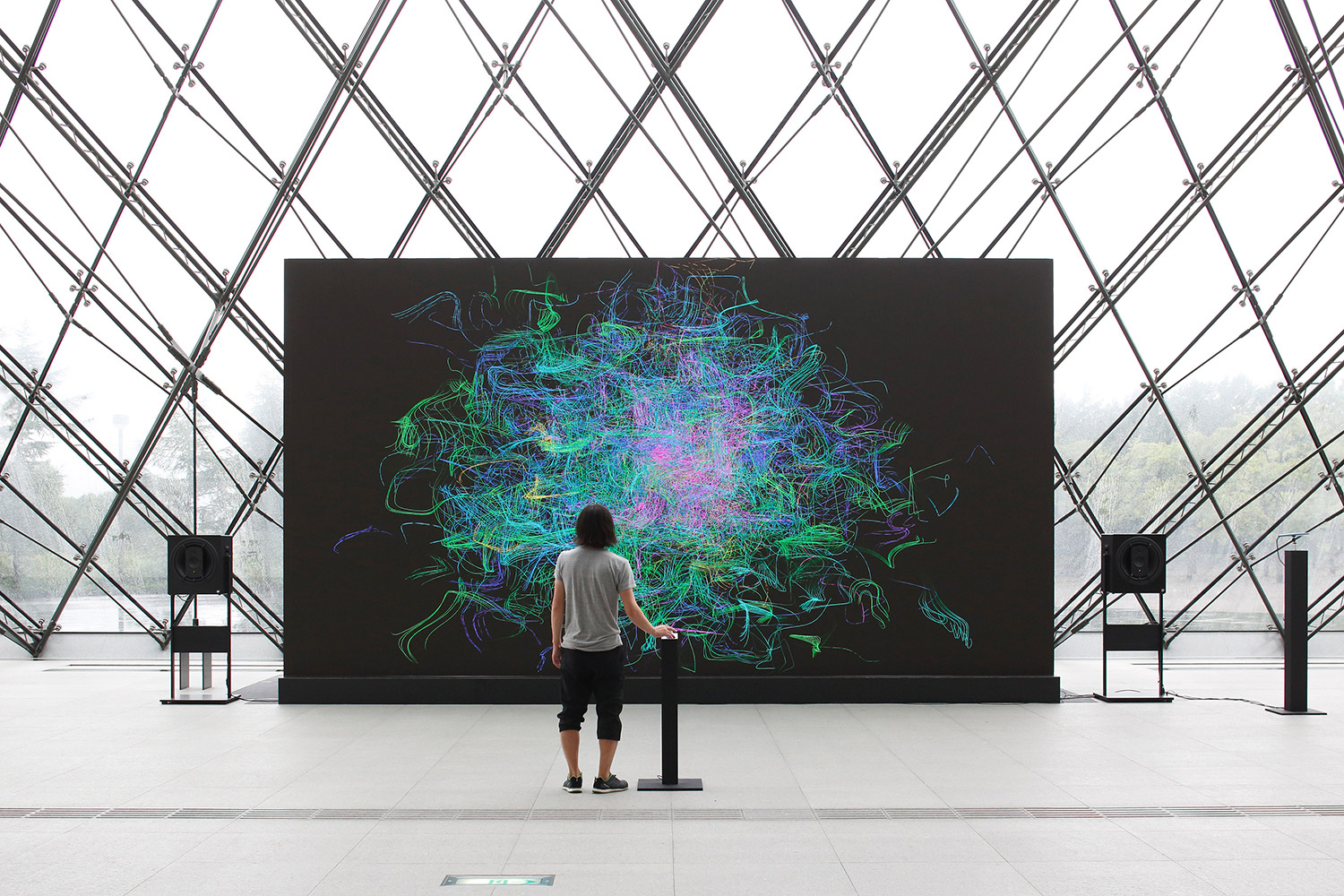 The exhibition image for Sensing Streams features a man standing in front of a large monitor with his right hand on a controller.