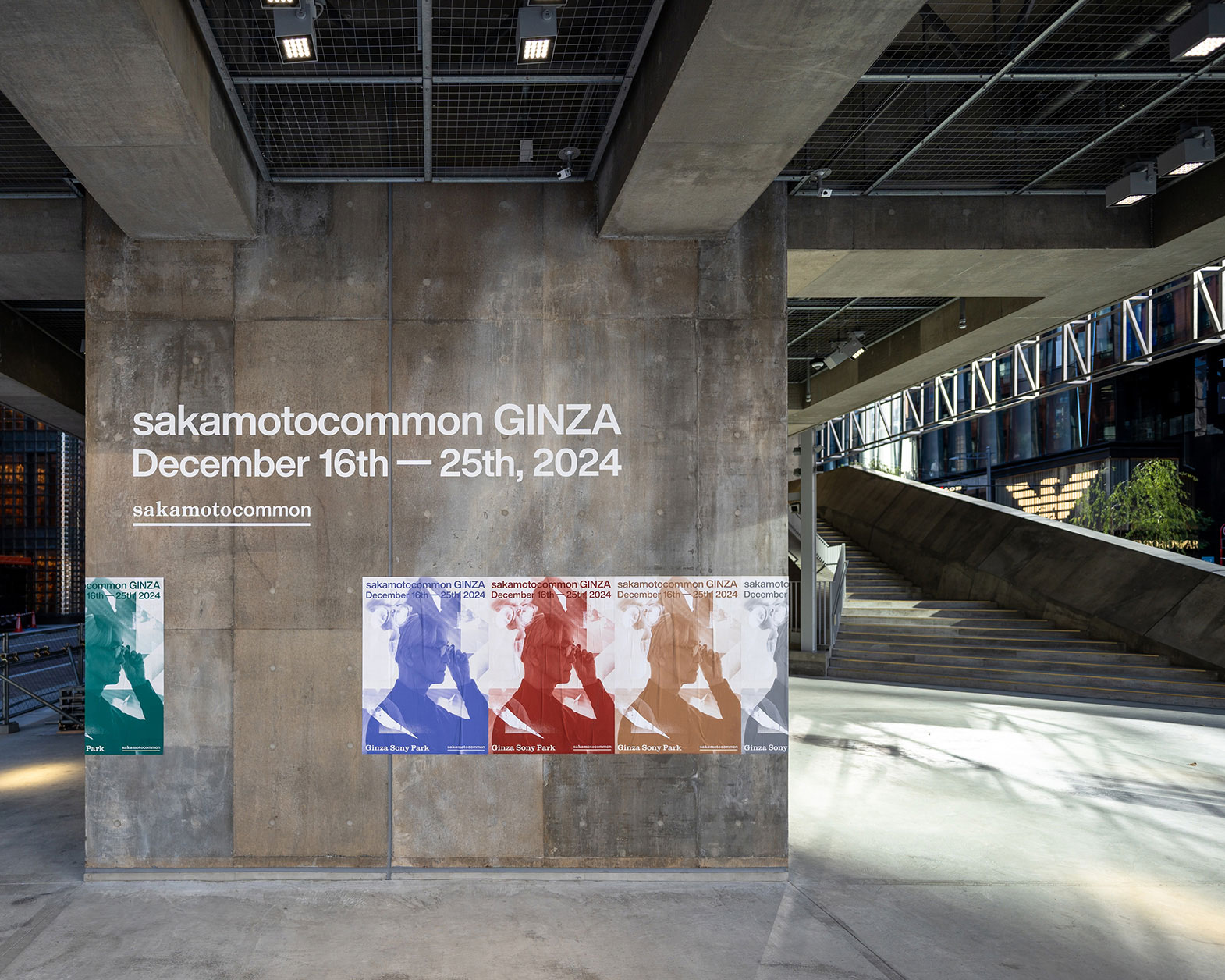 On the concrete wall, there are signs and posters for "sakamotocomon GINZA."