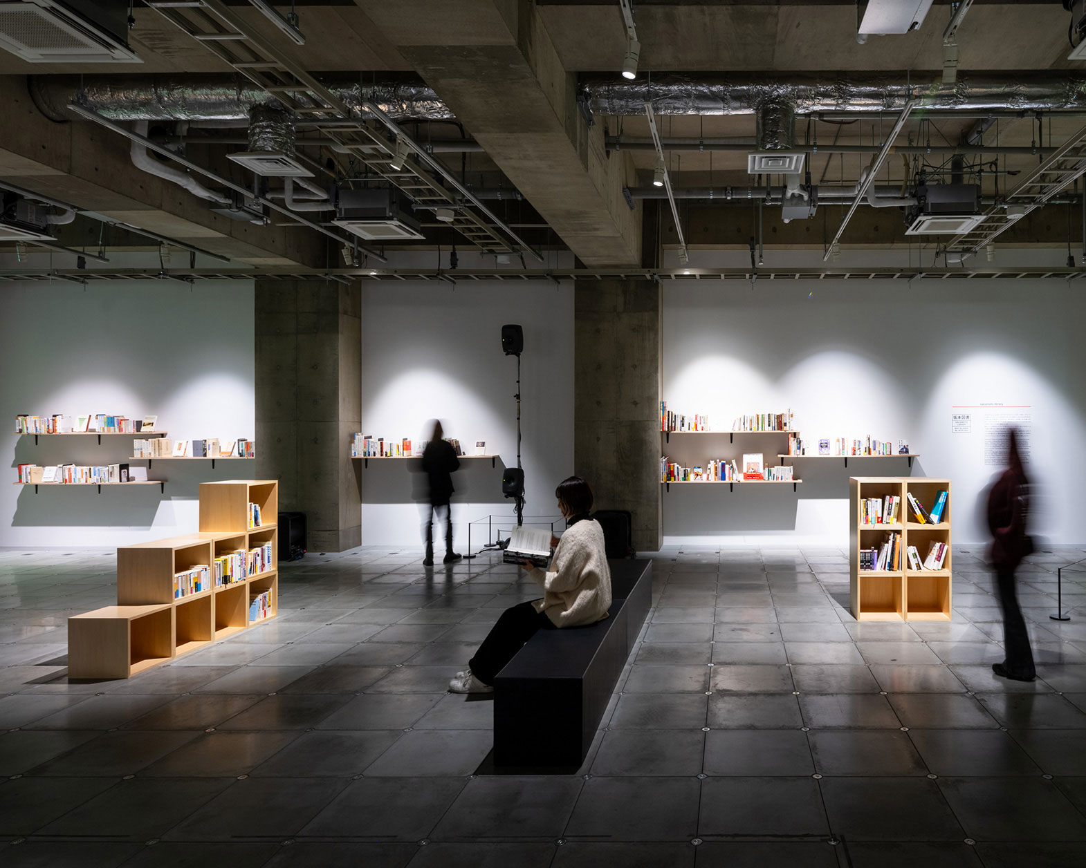 Various bookshelves are lined up on the floor, with people standing or sitting and reading books.