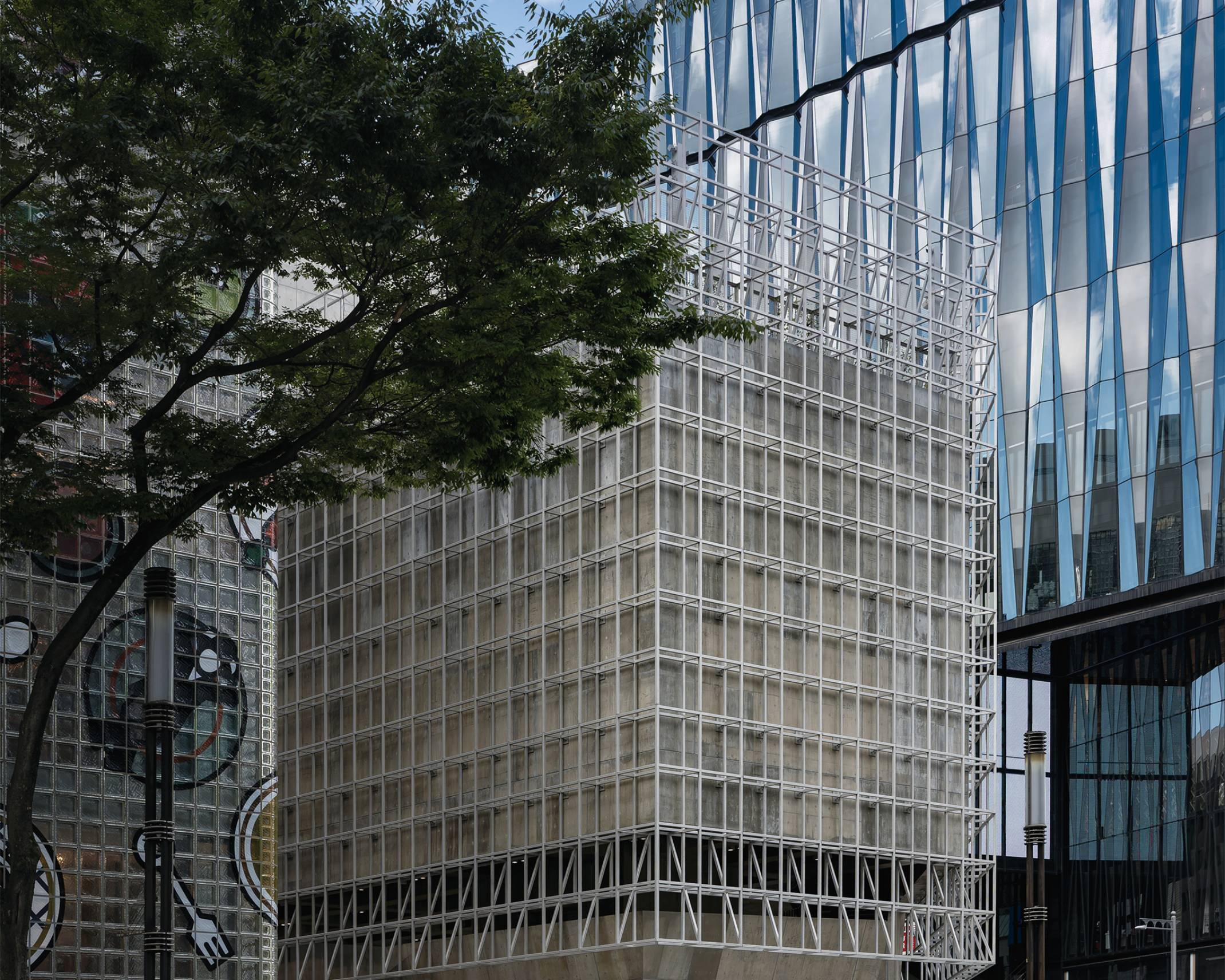 Exterior. Ginza Sony Park, with its low height and grid-like façade, is nestled between Maison Hermès and Tokyu Plaza Ginza. Trees line the street in front of it.