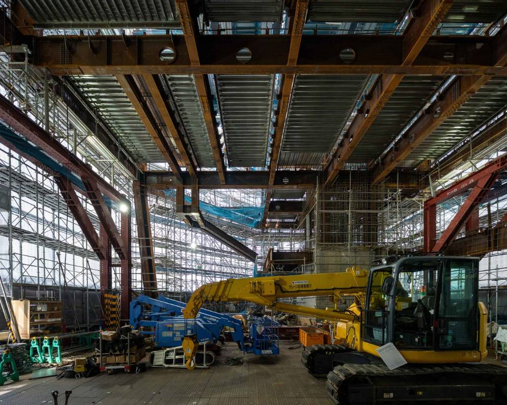 Interior. The above-ground atrium space, surrounded by the temporary construction fence and scaffolding. The roof has a steel frame built into it, and on the ground there is heavy construction equipment.