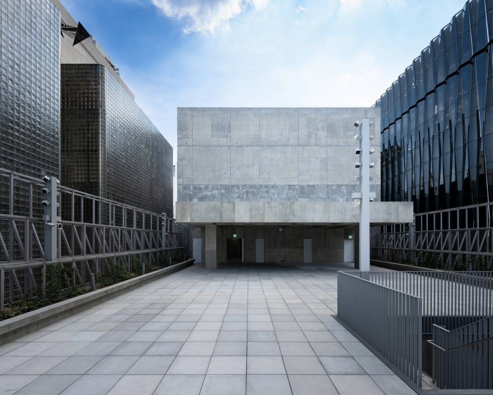 Exterior. The rooftop floor, nestled low compared to the surrounding buildings, with its concrete tower and pavilion beneath the blue sky.