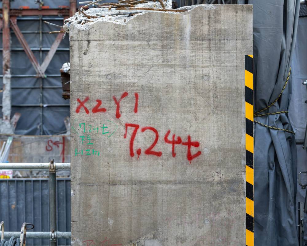 Close-up. Beam from the old building frame, cut out during the demolition process. The beam has “7.24 tons” written on it in red spray paint.