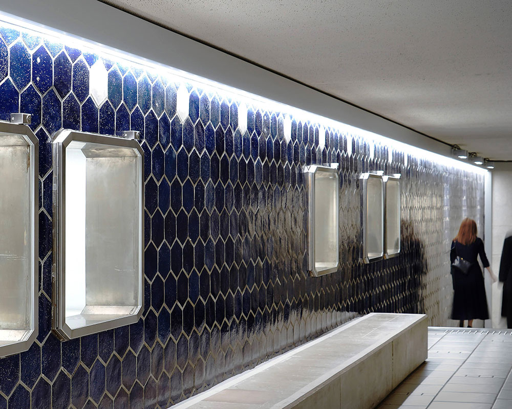 A man and a woman are descending the stairs behind a showcase with blue tiled walls.