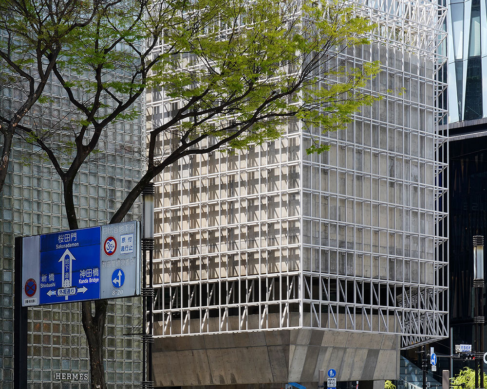 Fresh green street trees and the exterior of Ginza Sony Park are visible behind a person waiting at a crosswalk.