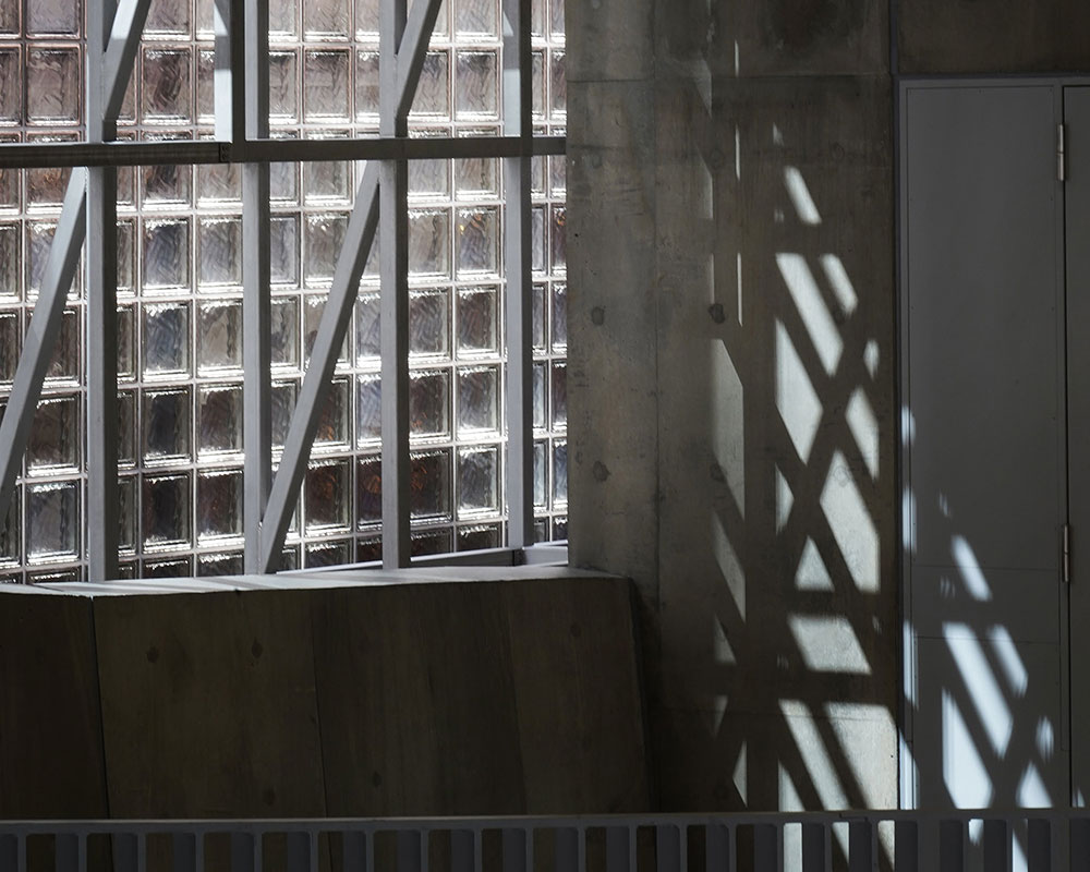 Sunlight streams in. Grid-like shadows from the framework fall on the interior concrete walls.