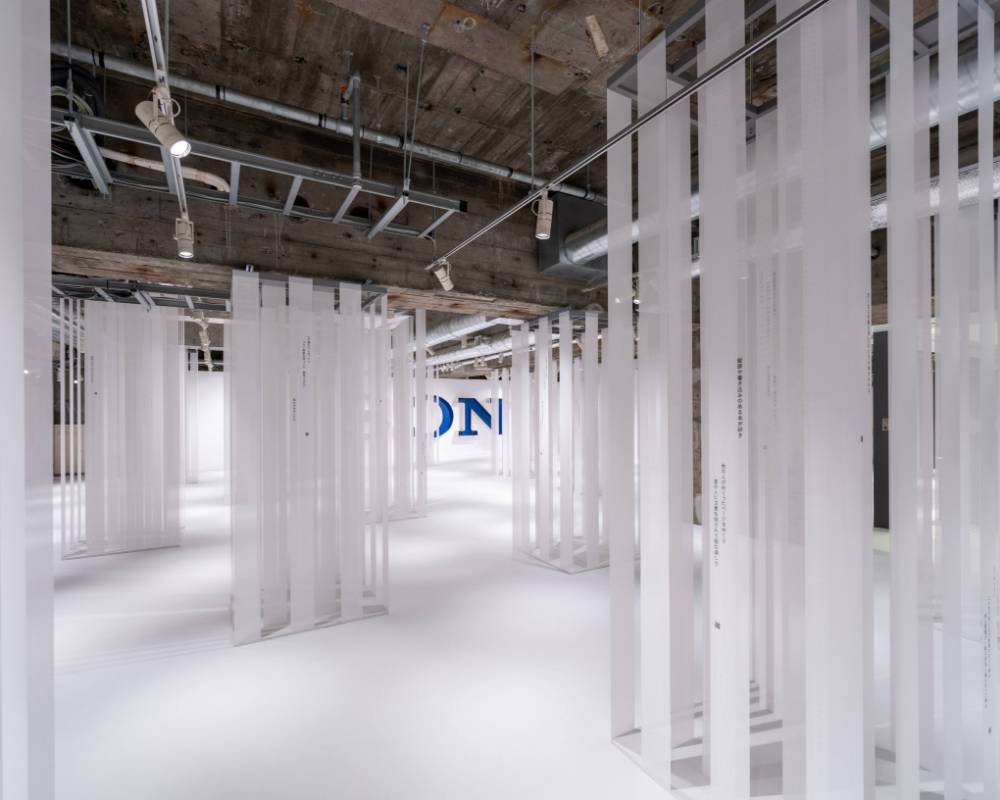 Exhibit. Many strips of white cloth hang from the ceiling, like trees in a forest, in an underground space. Each strip of cloth is printed with dialogue from a film.