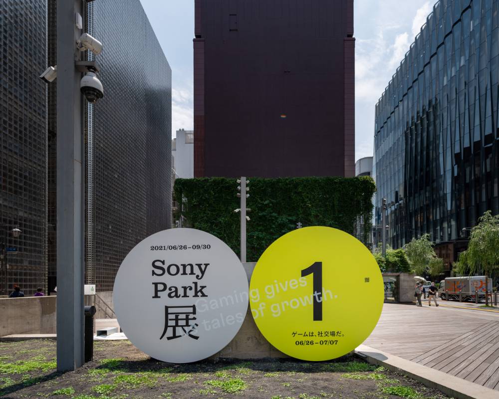 Exterior. A round gray art object with the main visuals of the exhibition, and a yellow version of the same object labeled “1,” are displayed side by side on the ground floor.