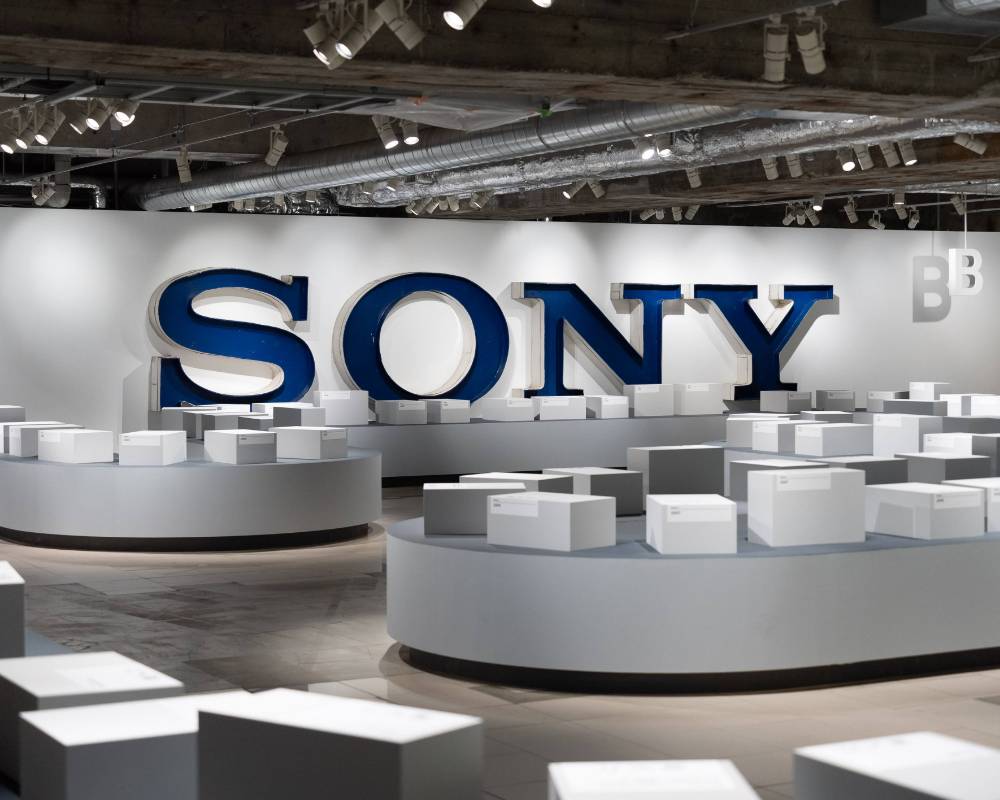 Exhibit. 100 or so white boxes are displayed in a venue that looks almost like an airport baggage claim. On the back wall is a sign that says “SONY.”
