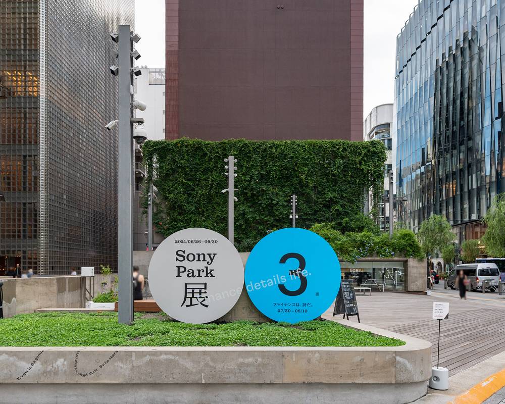 Exterior. A round gray art object with the main visual of the exhibition, and a blue version of the same object labeled “3,” are displayed side by side on the ground floor.
