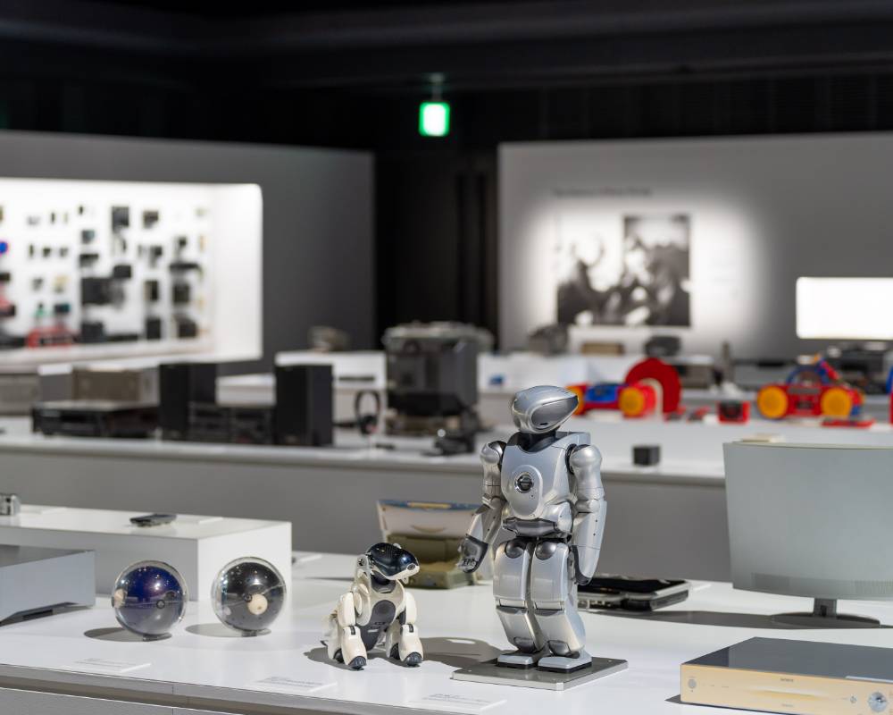 Exhibit. The entertainment robot aibo, small biped entertainment robot QRIO, and spherical Q.taro are exhibited on the display stand in the foreground.
