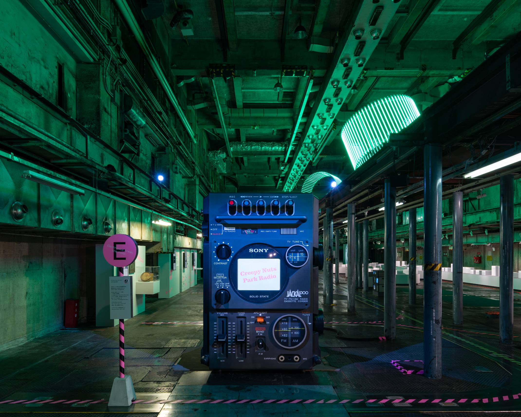 Exhibit. An exhibit of a giant radio cassette recorder art object with an integrated TV, in a space lit with green lighting.