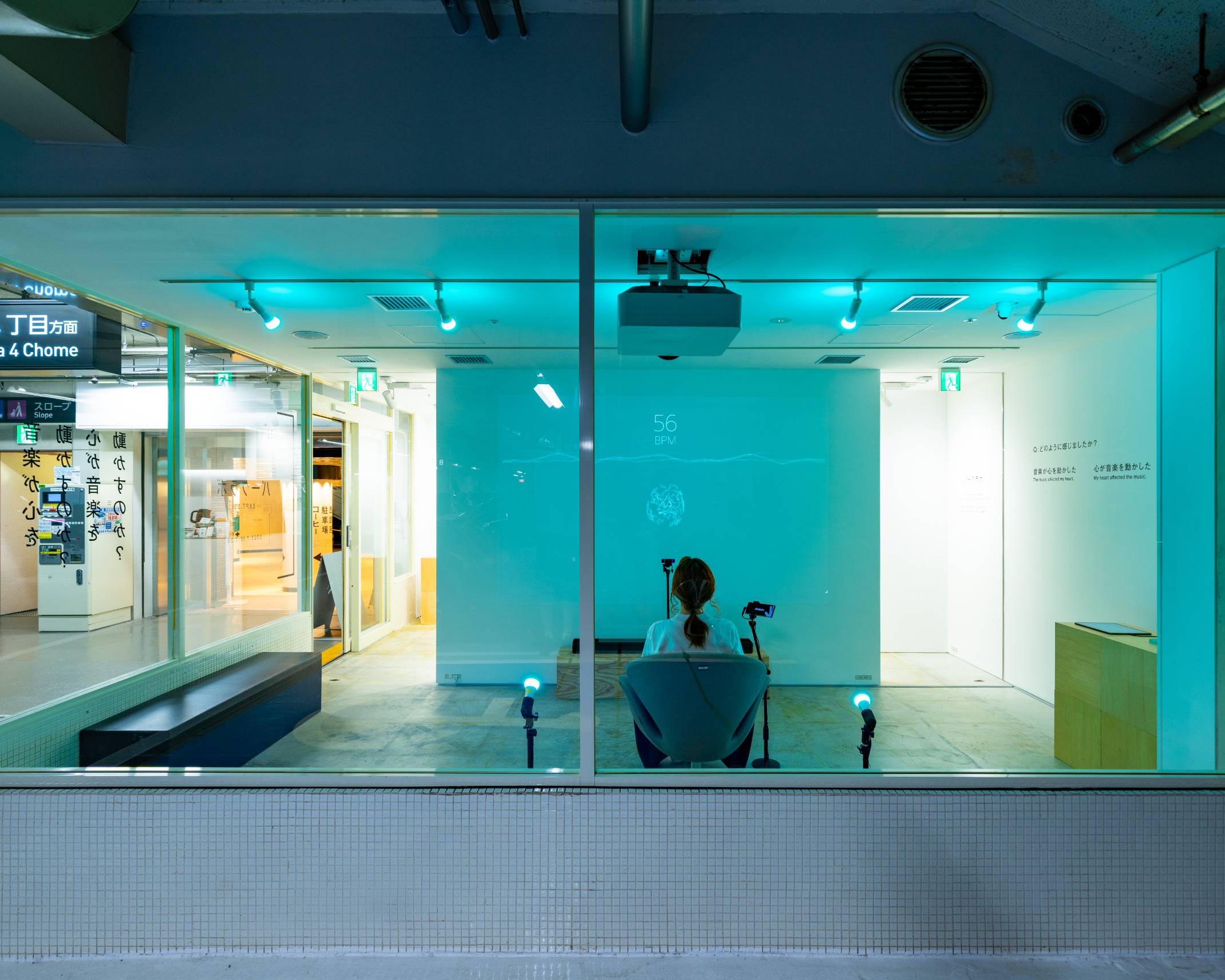 A hands-on experience. A visitor sits in a chair, with a video projected on the wall in front of her. The entire space has been lit blue by the lighting.