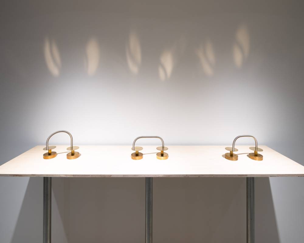 Exhibit. A display of three art pieces, each comprised of a metal spring and circles, with the light reflected on the walls changing according to the movement of the springs.
