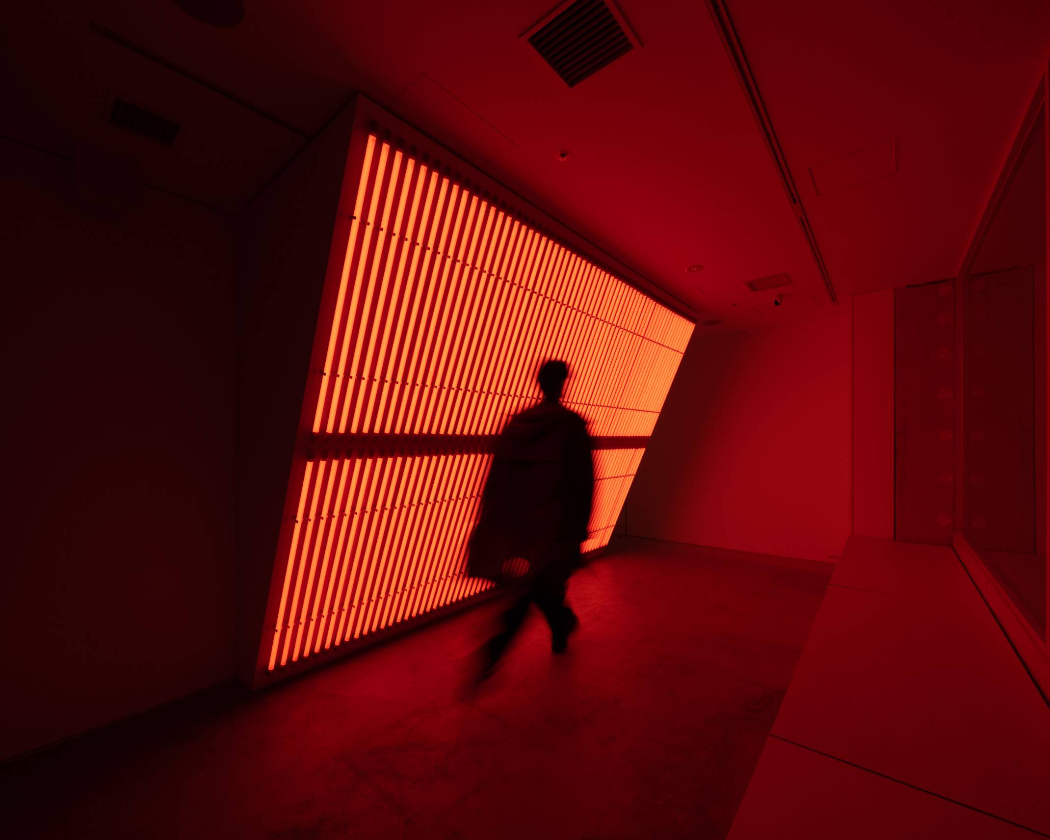 Interior. A person walks in front of an art installation with orange-colored light.