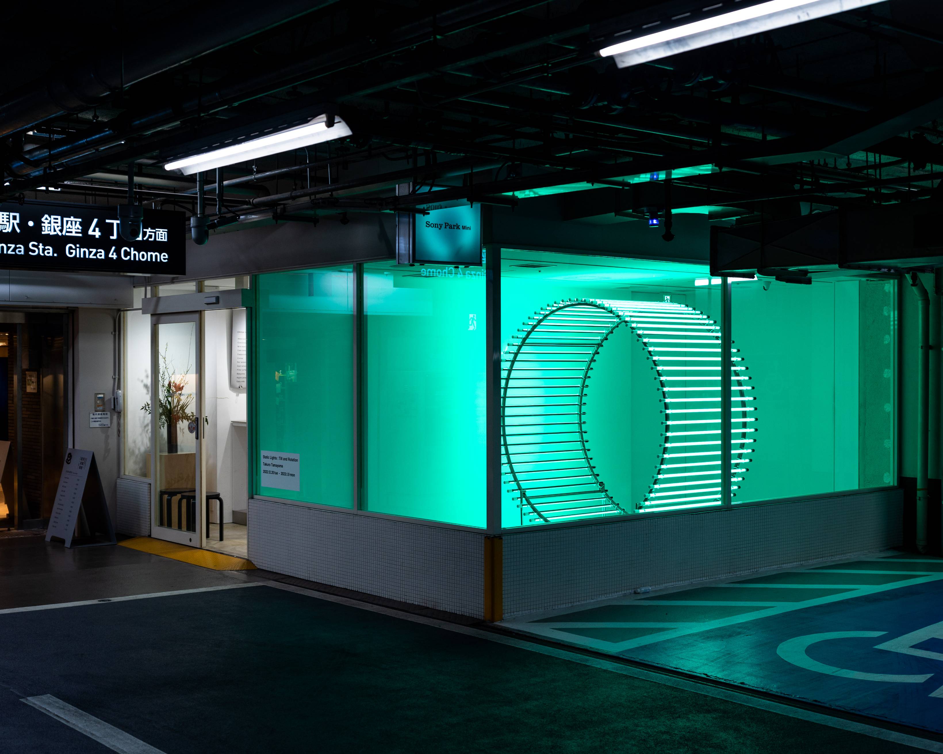 Exterior. A cylindrical object bathed in green light is displayed within the exhibition space.