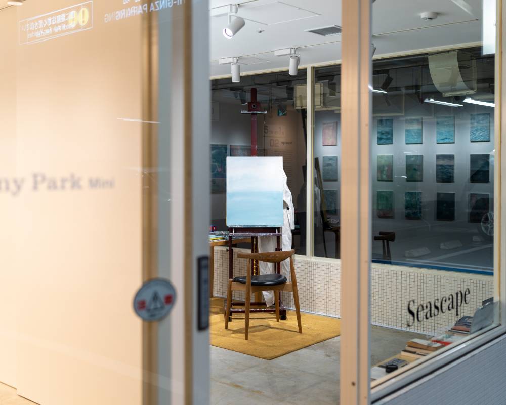 Exterior. The exhibition space features a painting on an easel and a chair, both of which can be seen from the entrance