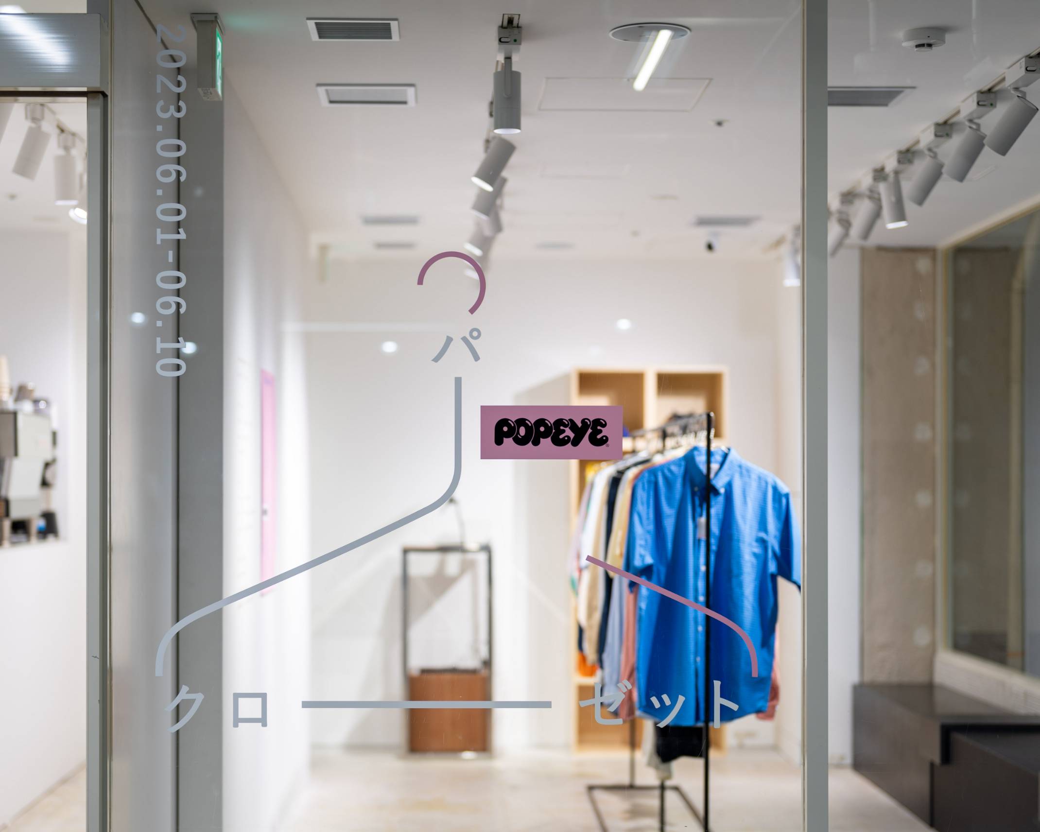 Exterior. A hanger-like graphic with the POPEYE logo is displayed on the glass window of the exhibition space, and in the center of the space is a hanger rack hung with various items of clothing.