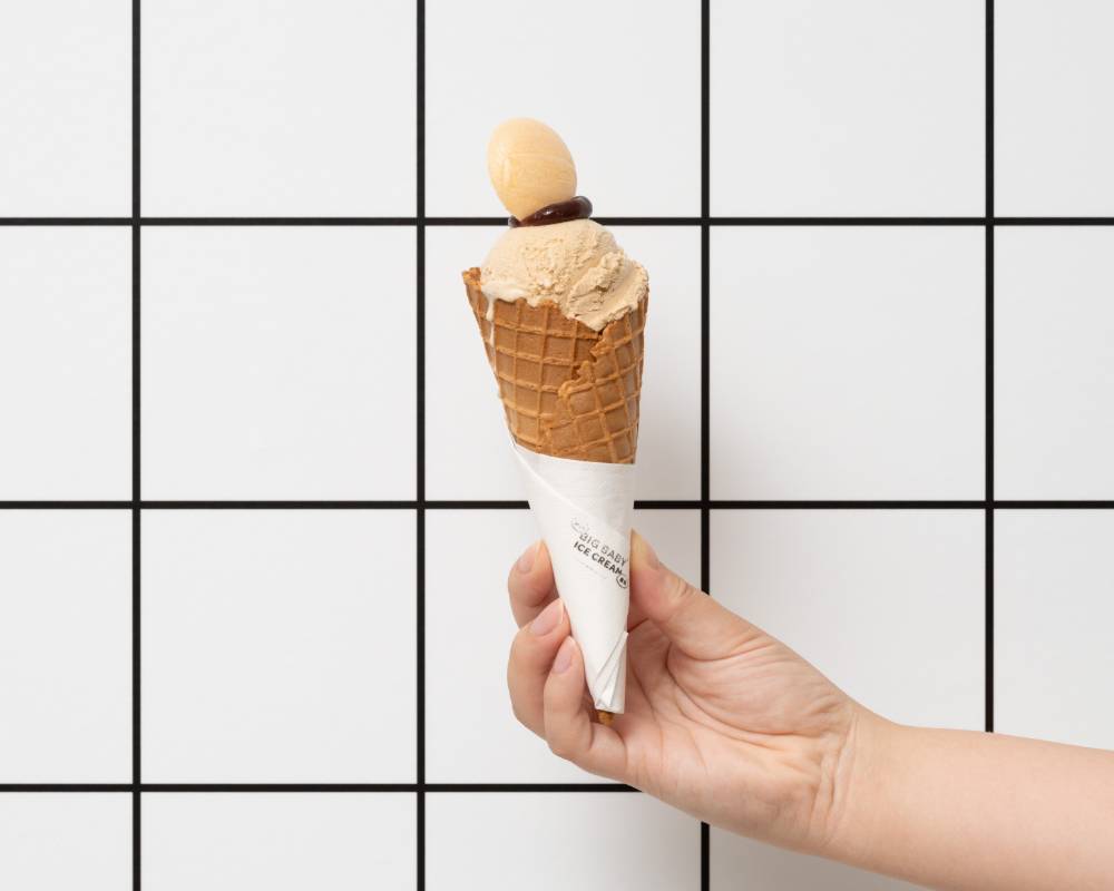Product. A person holds a mocha-colored ice cream in a cone in their right hand, in front of a grid-patterned wall.
