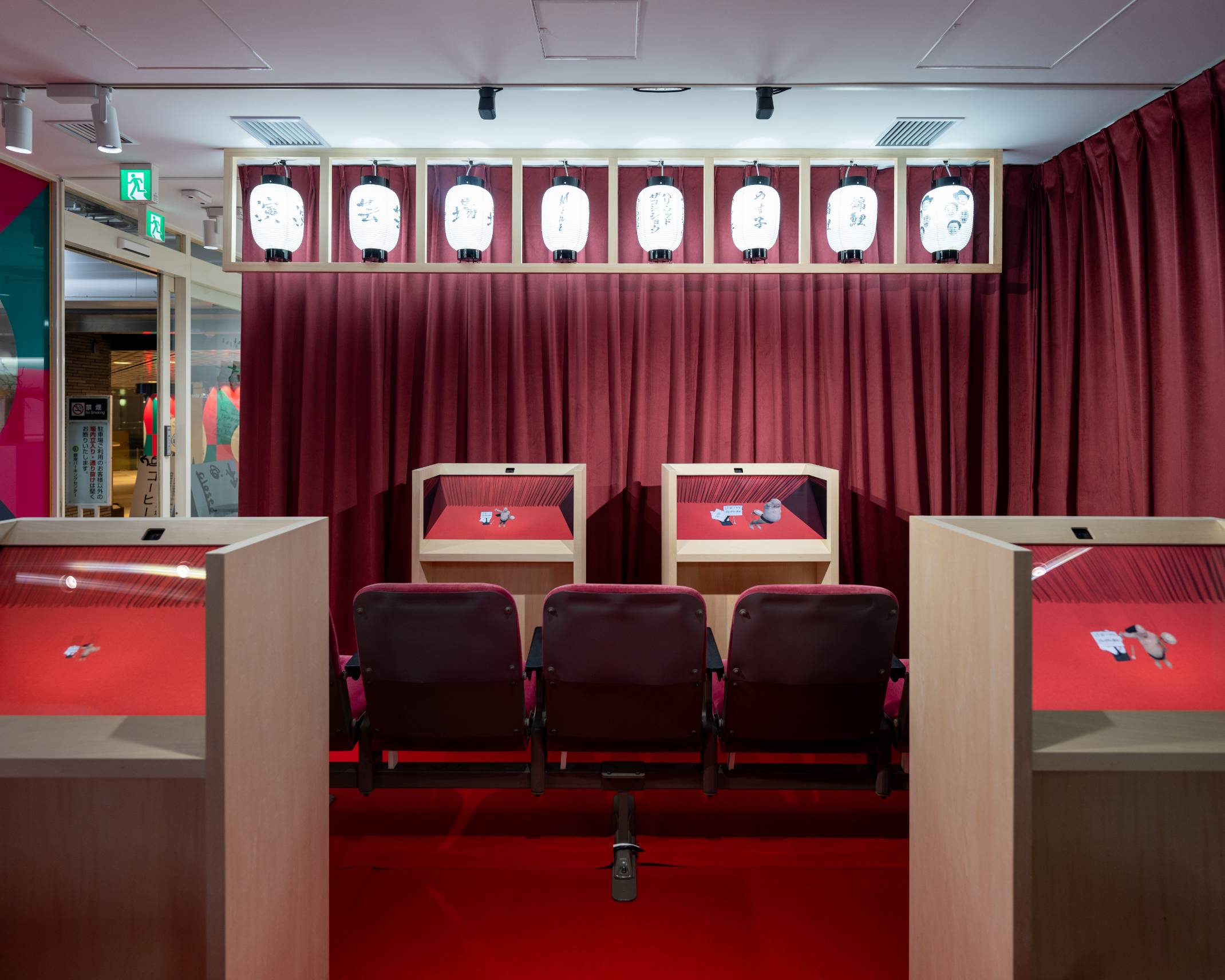 Interior. The inside of the space, which is decorated with burgundy-colored curtains and lanterns, features rows of monitors, each embedded within a wooden stand.