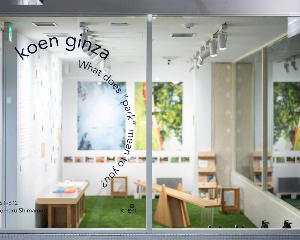 Exhibit. In the exhibition space, there are photos on the wall, and there are wooden pieces of furniture designed to look like playground equipment sitting on the floor, which is covered with green turf.