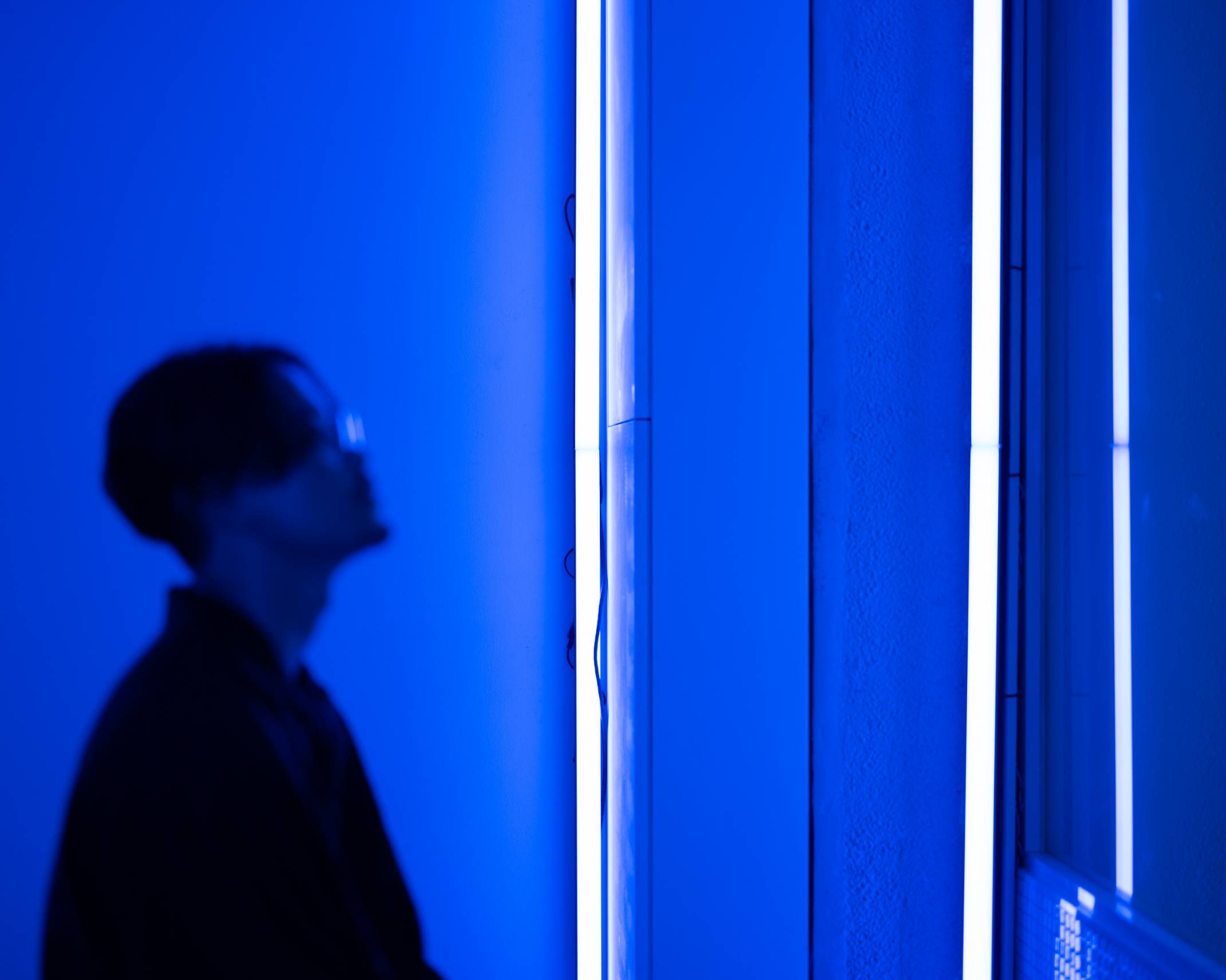A hands-on experience. A visitor looks up slightly in the space, which has been lit up blue from the light of the two vertically-placed line lights.