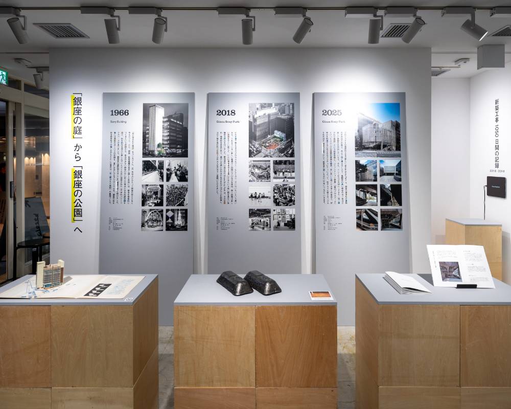 Exhibit. Three vertical panels line the wall, with three platforms in front of them displaying booklets and pieces of metal.