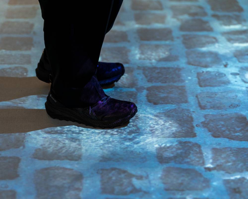 A hands-on experience. A person walks on top of a projection of brick paving stones with water collected in the cracks.