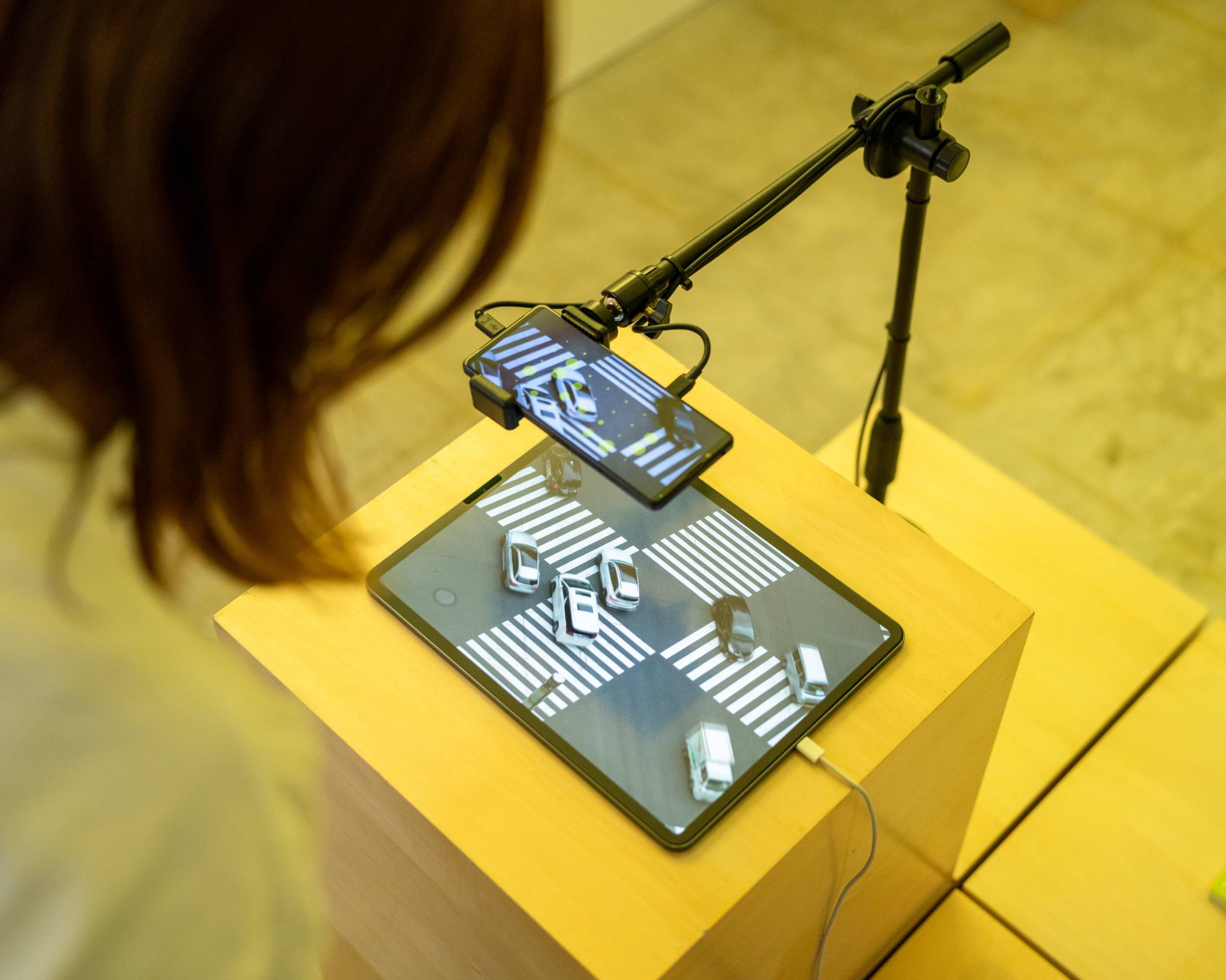 A hands-on experience. A person looks on as a smartphone camera detects a video of an intersection displayed on a tablet.