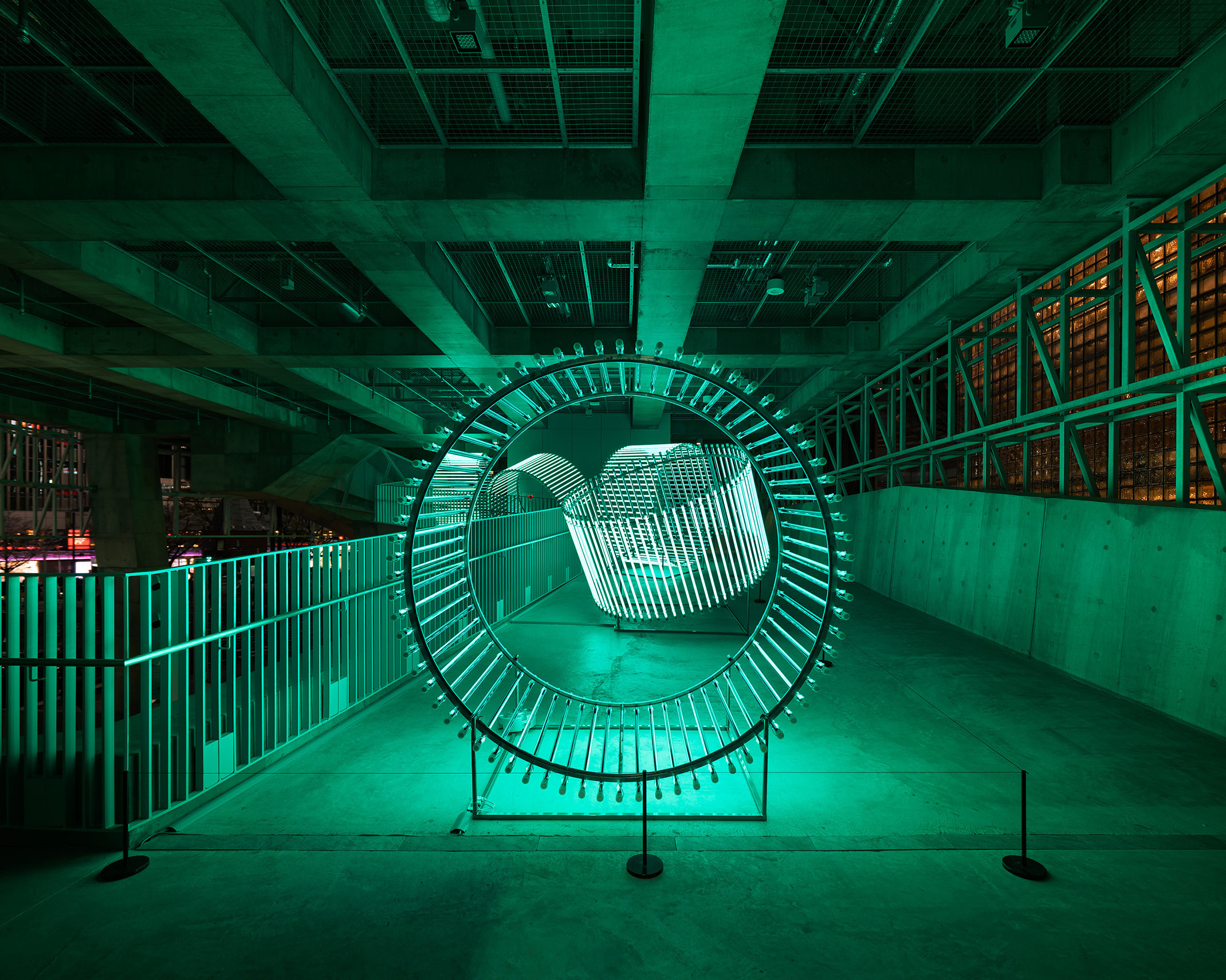 Exhibit. Green ring-shaped lights glow in a concrete architectural space.