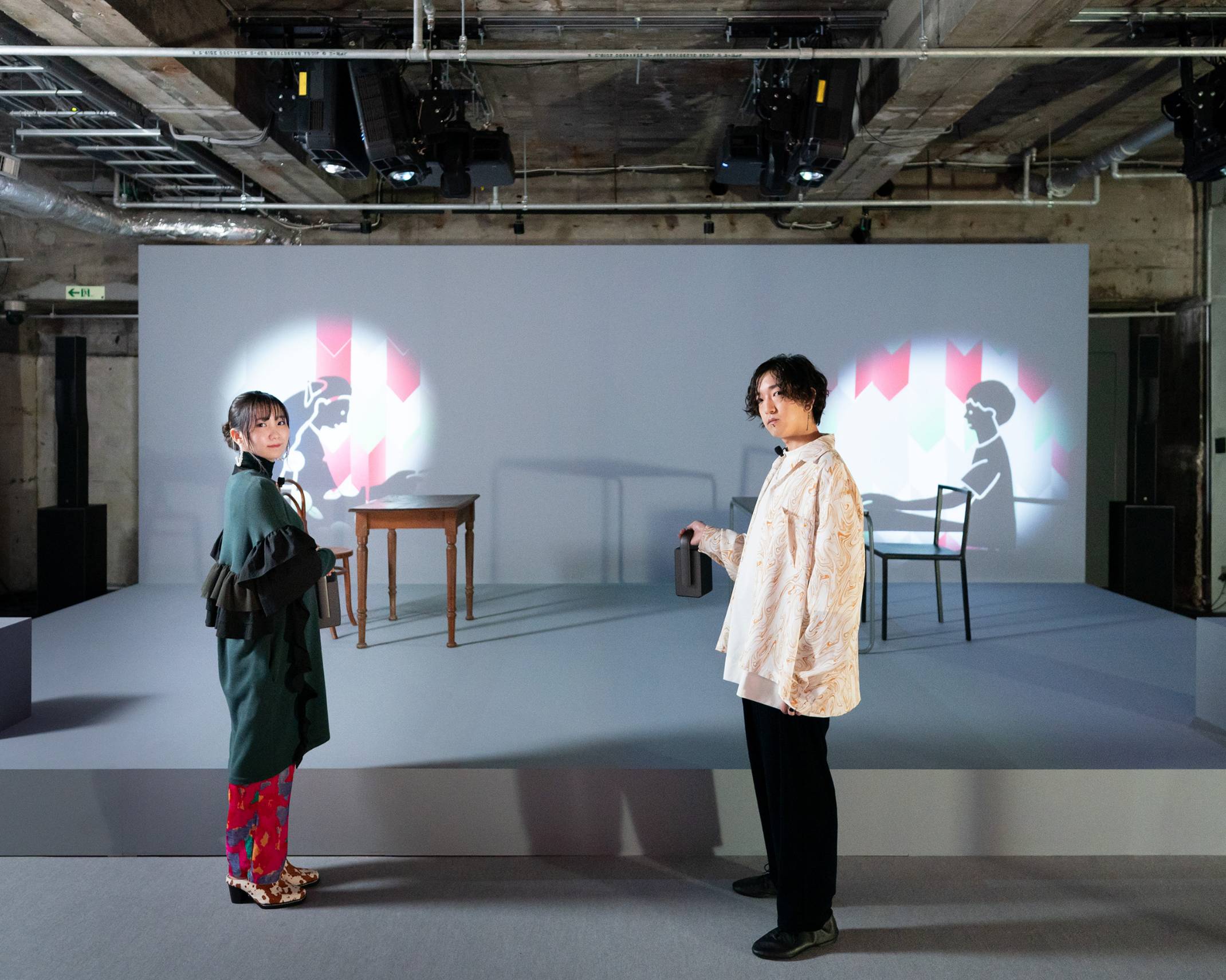 A hands-on experience. The two members of YOASOBI experience the exhibit, which consists of shadow puppet animations that appear when the walls are illuminated with special electric lights.