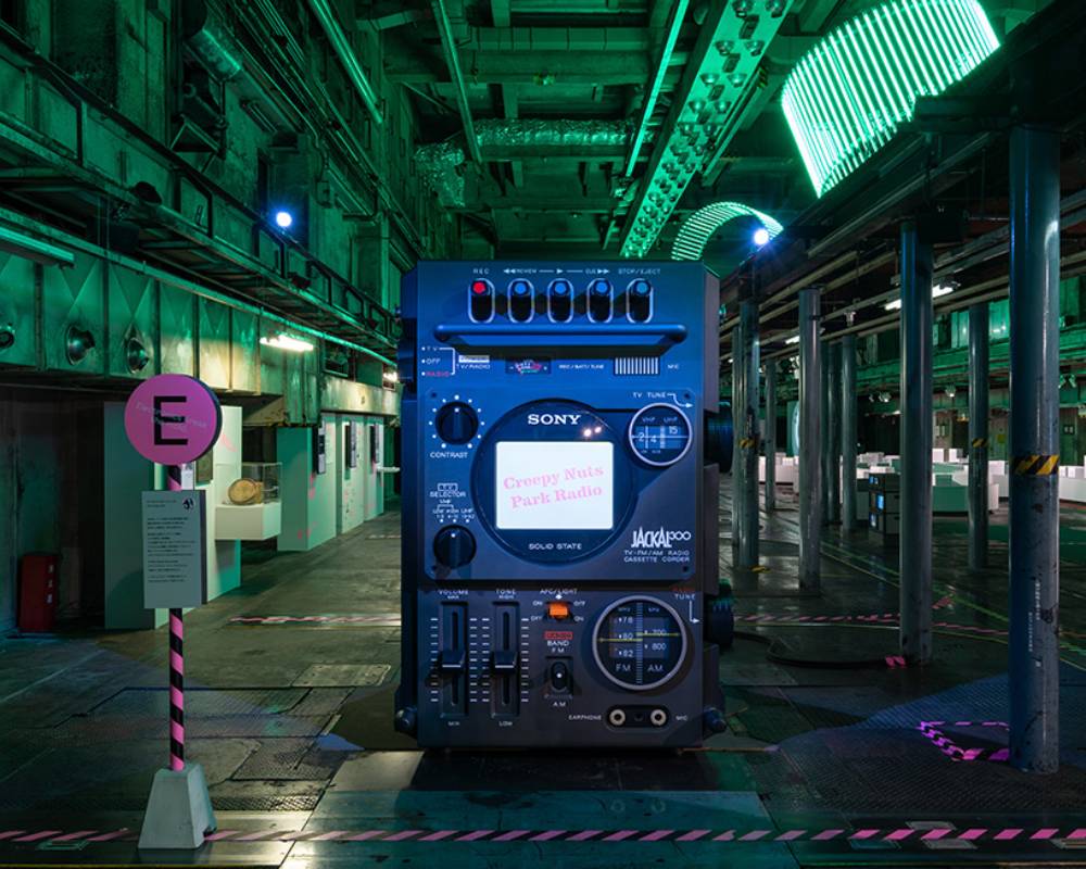 Exhibit. An exhibit of a giant radio cassette recorder art object with an integrated TV, in a space lit with green lighting.