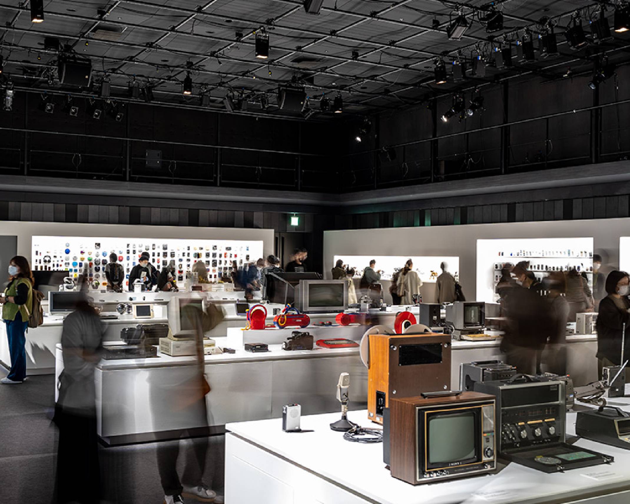 Exhibit. An exhibit of many past Sony products, with Trinitron color TVs on the exhibition stand in the foreground, My First Sony products near the center, and WALKMAN models on the back wall.