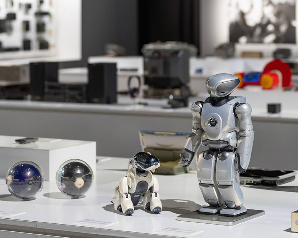 Exhibit. The entertainment robot aibo, small biped entertainment robot QRIO, and spherical Q.taro are exhibited on the display stand in the foreground.