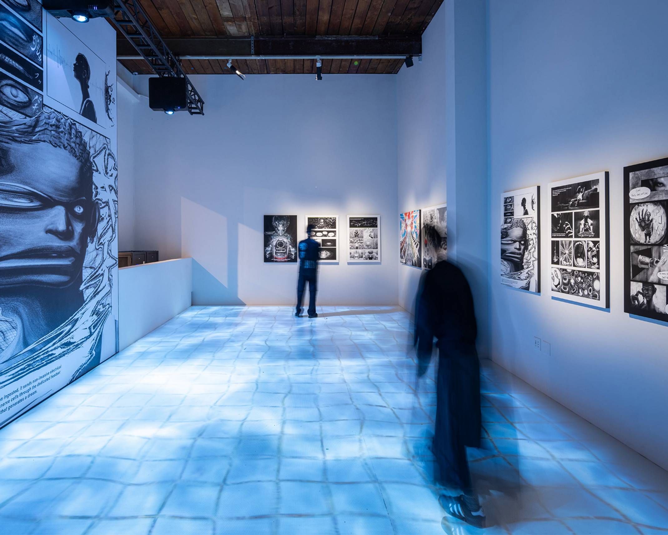 Exhibit. Individual pages from the manga DREAM PILL are exhibited on the walls, and an image of tiles covered in water has been projected onto the floor.