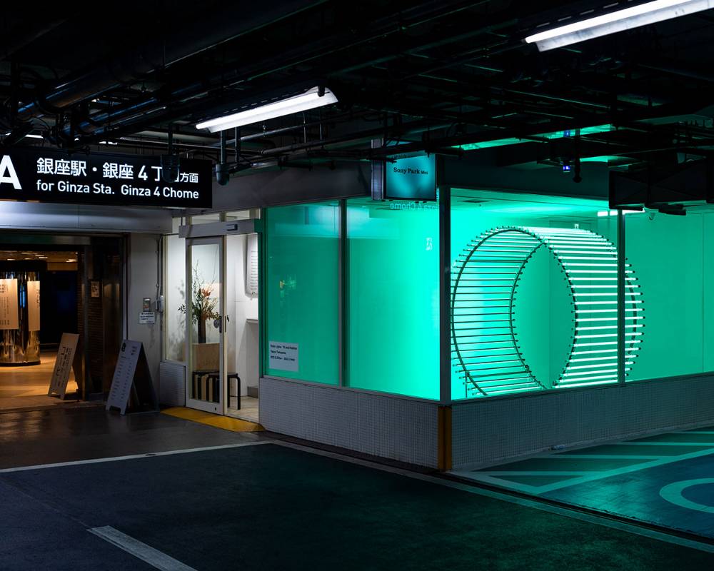 Exterior. A cylindrical object bathed in green light is displayed within the exhibition space.