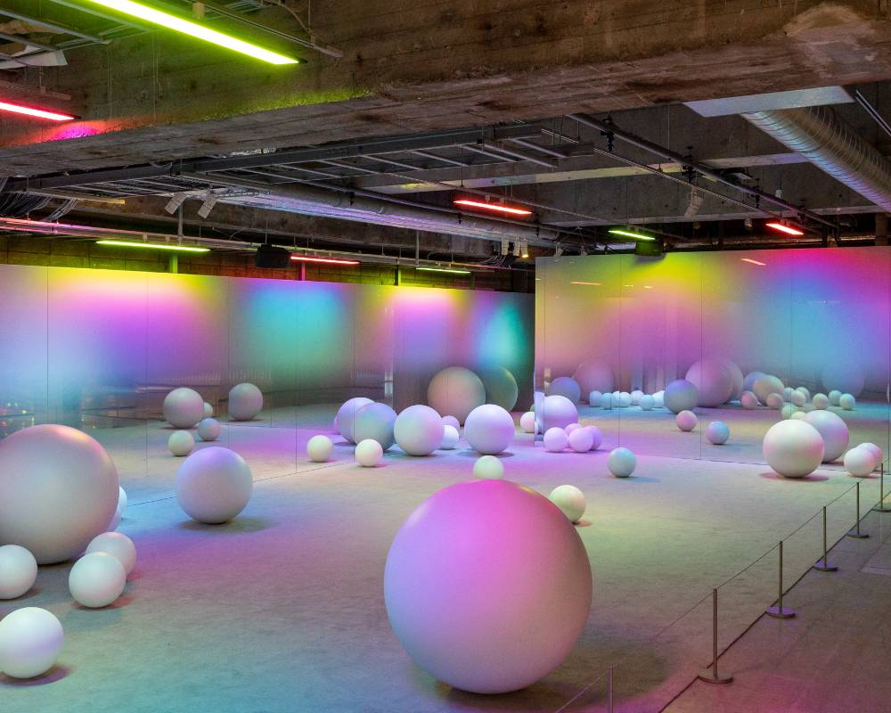 Exhibit. Spheres of various sizes are scattered in a space filled with colorful light.