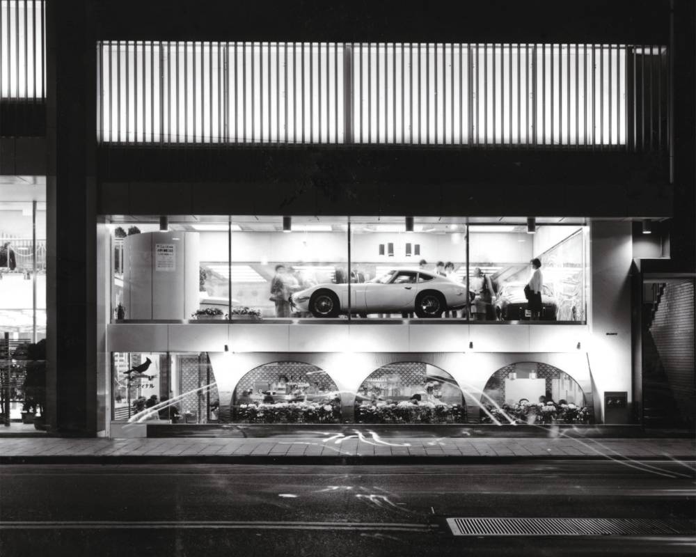 Exterior (black-and-white). On the first floor on the Sotobori Street side of the building is a coffee shop, and there are cars displayed along the second-floor window.